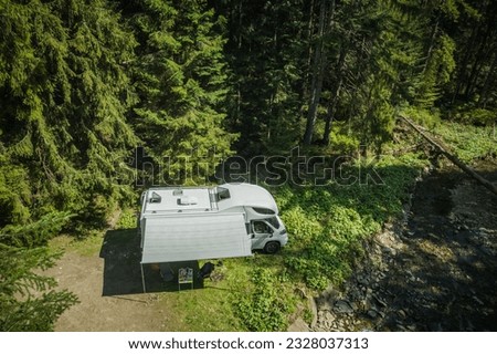 Aerial View of White Camper Van Parked Solo in the Forest Next to Woodland Stream. RV Camping and Traveling Theme.