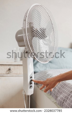 female hand includes button on electric fan of air conditioner for cooling in summer heat, malaise during summer heat, high air temperature. cooling and humidification of indoor air. heat stroke Royalty-Free Stock Photo #2328037785