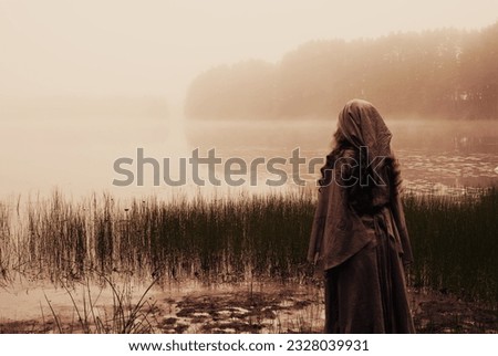 Shaman woman looking out over misty lake. Haunting landscape evokes Norse Mythology or pagan mysticism.   Royalty-Free Stock Photo #2328039931