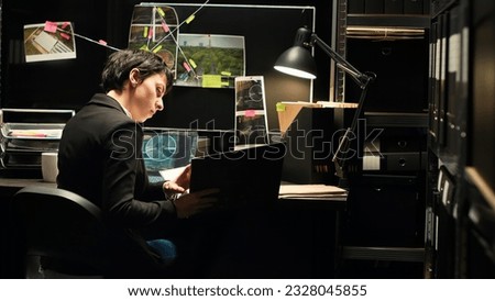 Detective gathering intelligence using surveillance photos and classified documents in criminal case file. Police expert conducting investigation to uncover new information, forensic science. Royalty-Free Stock Photo #2328045855