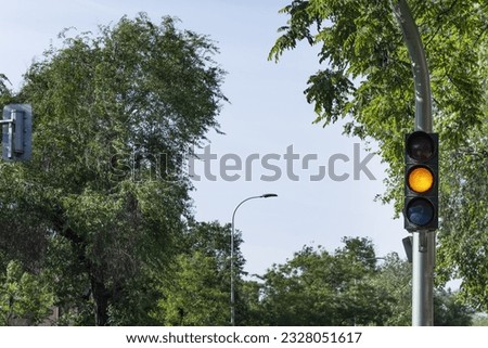 A traffic light with amber light on a street with leafy trees