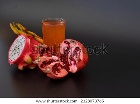 A glass of tropical fruit juice on a black background, next to pieces of ripe pitaya and a broken pomegranate fruit. Close-up.