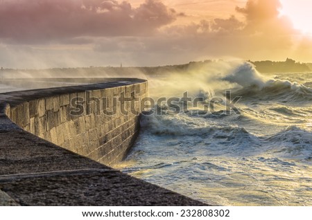 Big waves crushing on curved stone pier, on stormy weather with vivid sunset, big tide, Saint Malo, France. Royalty-Free Stock Photo #232808302