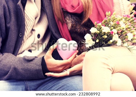 A midsection of a romantic couple sitting on a bench in the park holding Valentines gift and flowers Royalty-Free Stock Photo #232808992