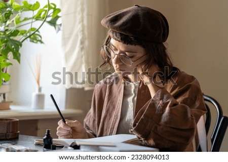 Concentrated artist young woman drawing in notebook with black ink at table in cozy art studio workshop. Sad, depressed teen girl painting from mental health problems. Art therapy for stress relief.