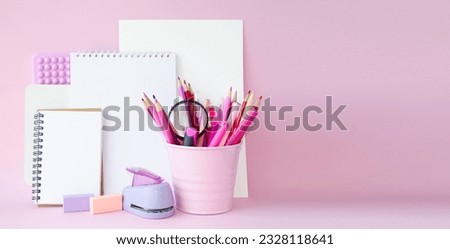 On the table on a pink background are pink school supplies, pencils, felt-tip pens, an eraser, notepads and notebooks with white sheets.  Banner, copy space for text.  Concept back to school.