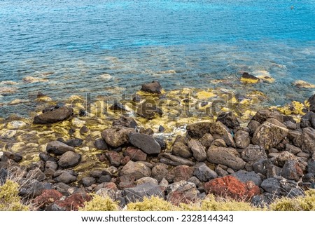 View fron the top of a beautiful volcanic rocks and reefs on a shallow and clear water by the cliff in a blur foreground of dry grass in the Santorini island