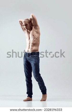 Full-length portrait of handsome young man with blonde hair, musuclar body posing shirtless in jeans over grey studio background. Concept of male natural beauty, body care, health, sport, fashion, ad Royalty-Free Stock Photo #2328196333