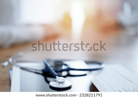 Stethoscope and tablet computer are lying on the wooden table while doctor and patient discussing something at the background. Medicine concept