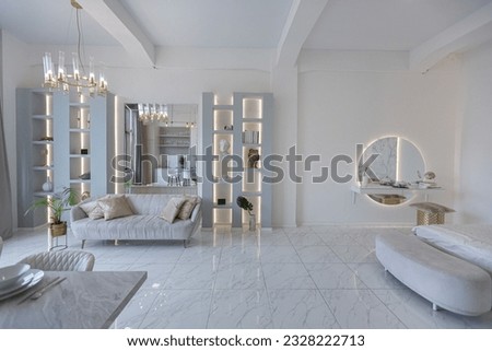 minimalistic light elegant luxury design of a modern spacious studio apartment with kitchen area, bedroom and huge mirror behind the couch. tiles on the floor and high ceiling. Royalty-Free Stock Photo #2328222713