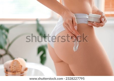 Young woman applying anti-cellulite cream onto her buttocks in bathroom, closeup Royalty-Free Stock Photo #2328227795