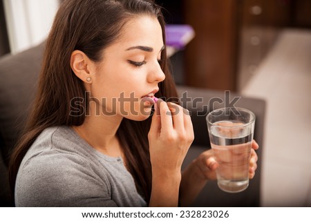Cute young brunette taking a pill with a glass of water at home Royalty-Free Stock Photo #232823026
