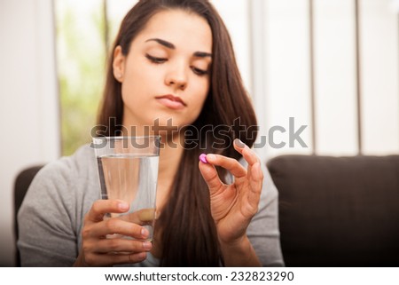 Pretty young woman holding a morning after pill and a glass of water at home Royalty-Free Stock Photo #232823290