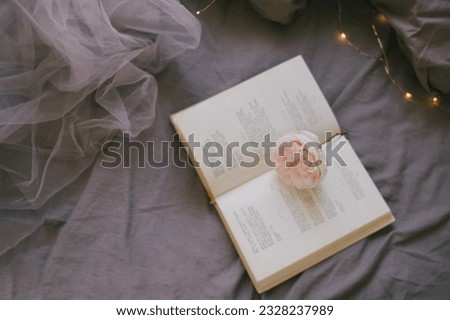 Open book and garden rose on a bed with natural vintage grey linen and lights on a background.