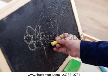 A close up portrait of a toddler scribbling, drawing or doodling a bit on a chalkboard. The child is writing on the blackboard and has a yellow piece of chalk in its hand.