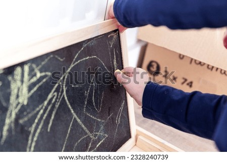 A portrait of a toddler scribbling, drawing or doodling a bit on a chalkboard. The child is writing on the blackboard and has a yellow piece of chalk in its hand.