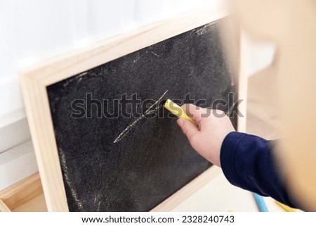 A close up portrait of a toddler scribbling, doodling or drawing a bit on a chalkboard. The child is writing on the blackboard and has a yellow piece of chalk in its hand.