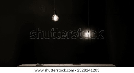 Two edison bulbs hanging from long cables with a black background and a curtain behind subtly illuminating a minimalist table with books on the surface forming an avant-garde and modern bookcase set.