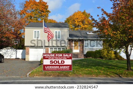 American flag pole Real Estate sold (another success let us help you buy sell your next home) sign suburban high ranch home autumn day residential neighborhood blue sky clouds USA