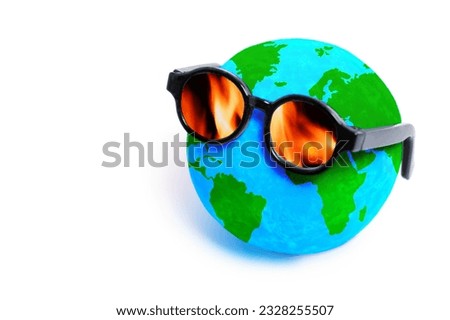 Globe model wearing sunglasses with lenses that reflect vibrant flames. Climate change, environmental activism and the need for sustainable solutions.
