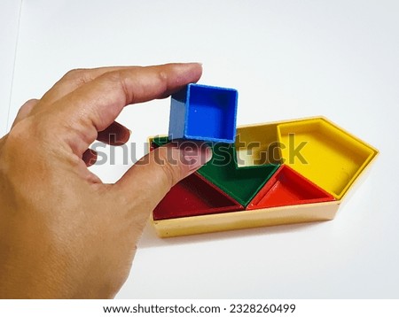 Vintage one way puzzle, colorful, 5 colored plastic pieces, 5 pieces placed on a white background. Hand holding a blue square puzzle piece.