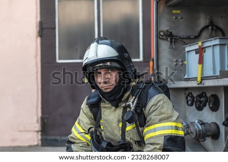 Portrait of a tired firefighter in a protective suit and a protective helmet sitting by a fire engine after returning to the fire department Royalty-Free Stock Photo #2328268007