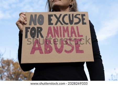 Woman holding placard sign with text No Excuse for Animal Abuse, during animals rights march. Protestor with cardboard banner at protest rally demonstration. Royalty-Free Stock Photo #2328269333
