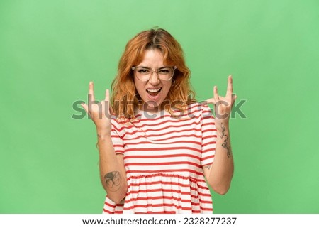 Young caucasian woman isolated on green screen chroma key background making horn gesture