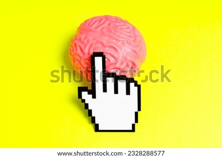 Plastic pixelated hand cursor clicks a pink human brain model isolated on a yellow background.