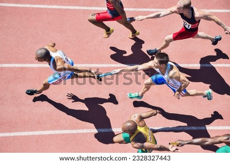 Relay runners passing batons on track Royalty-Free Stock Photo #2328327443