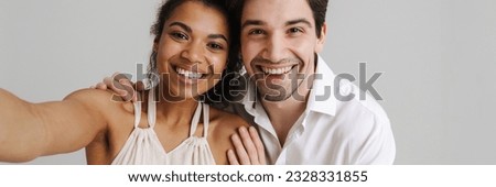 Happy young multiethnic couple in casual wear standing together isolated over gray background taking a selfie