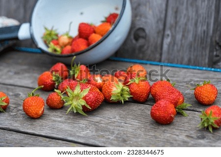 a cup with red strawberries, scattered berries on a wooden background
