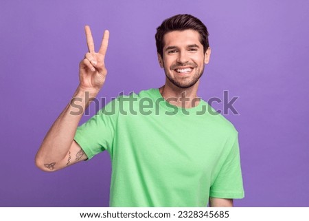Portrait of positive good mood nice guy with bristle wear green t-shirt showing v-sign say hello isolated on violet color background