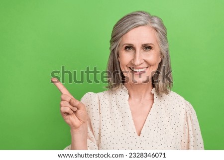 Photo portrait of lovely retired lady toothy smile finger point empty space dressed stylish white outfit isolated on green color background