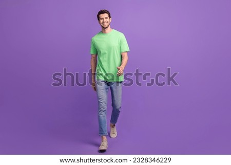 Full length body photo of young happy good mood guy walking bright green t-shirt denim jeans promo ad isolated on violet color background