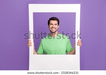 Funny young guy photographing through big white frame cadre memories capture wearing trendy t-shirt isolated on violet color background