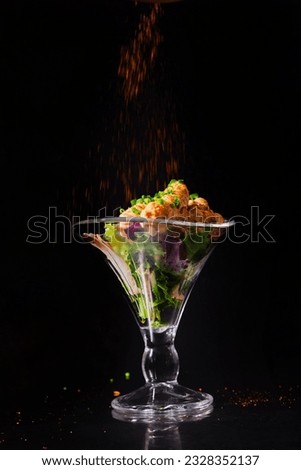 a bowl of shrimp stands on a black background and is sprinkled with red spices on top. commercial advertising photography