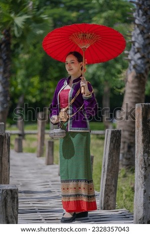Beautiful pretty young Asian woman wearing a millionaire traditional Thai dress Lanna style standing with an antique silver bag and umbrella in a green natural park. Portrait the old fashion costume. Royalty-Free Stock Photo #2328357043