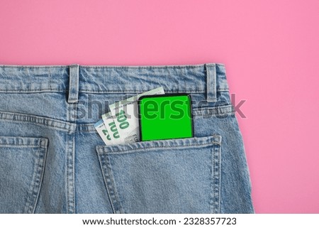 Smartphone green screen mockup and euro bills in back pocket of blue jeans on pink background. Banner with no people.