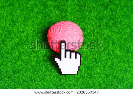 White blocky plastic pointer cursor clicks a pink human brain model placed on a green lawn background.