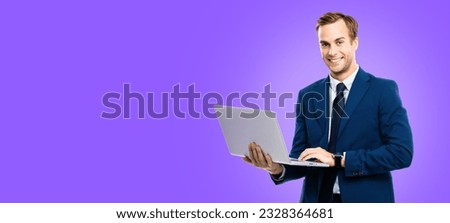 Smiling businessman in blue confident suit, working with laptop, over violet purple color background. Handsome young man at studio concept picture. Copy space.