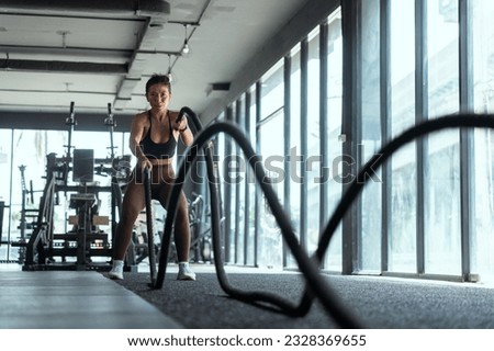 Woman with battle rope battle ropes exercise in the fitness gym. gym, sport, rope, training, athlete, workout, exercises concept Royalty-Free Stock Photo #2328369655