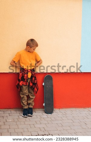 Outdoor activities for children. A cheerful young boy in bright clothes with a skateboard against the backdrop of a colorful wall. Caucasian schoolboy on a walk. Front view