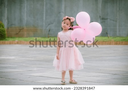 Cute little girl in pink dress taking pictures with balloons to celebrate her birthday.