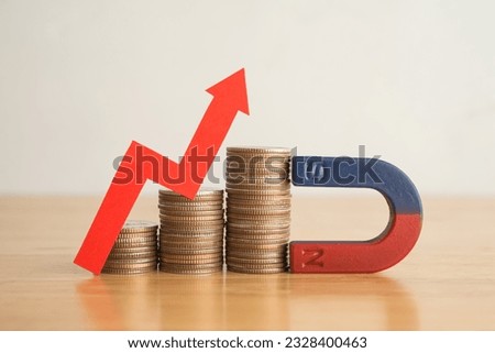 Magnet is attracting stacks coins with growth capital gains red graph chart on wooden table white wall background. Profit growth investment in stock market, funds, forex, etf, passive income concept.