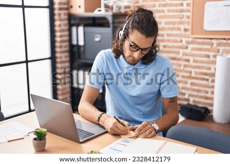 Young hispanic man call center agent writing on reminder paper at office