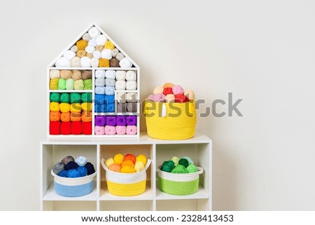 Shelving with storage baskets and colored balls of yarn for knitting. Bright yarn balls lined up on the shelves. Organizing and storage in craft room. Handmade, needle craft, creativity and  hobby.  Royalty-Free Stock Photo #2328413453