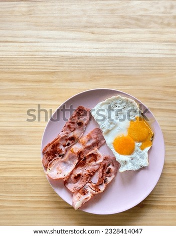 Pink plate of bacon and eggs on wooden table. Dedayuno, almuerzo.