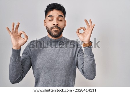 Hispanic man with beard standing over white background relaxed and smiling with eyes closed doing meditation gesture with fingers. yoga concept. 