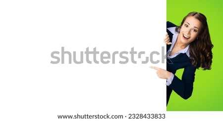 Happy excited woman in black confident suit showing pointing blank white banner signboard. Business and advertising concept. Copy space empty place for text. Green color background.	